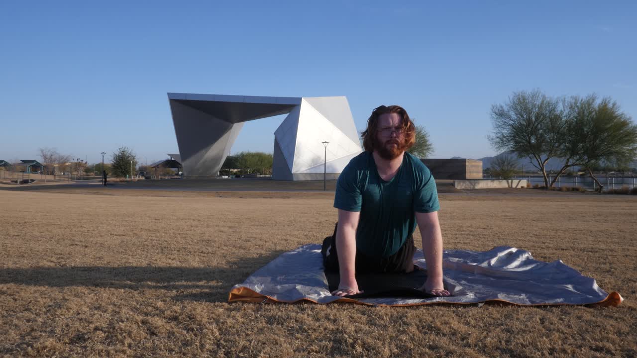 Red hair male stretching in a park with Gilbert amphitheater behind them.