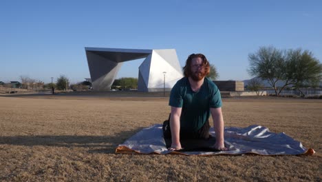 red hair male stretching in a park with gilbert amphitheater behind them.