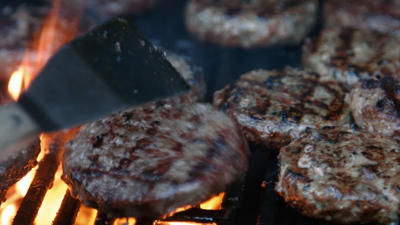 Chef che gira hamburger al barbecue con fiamme vivaci