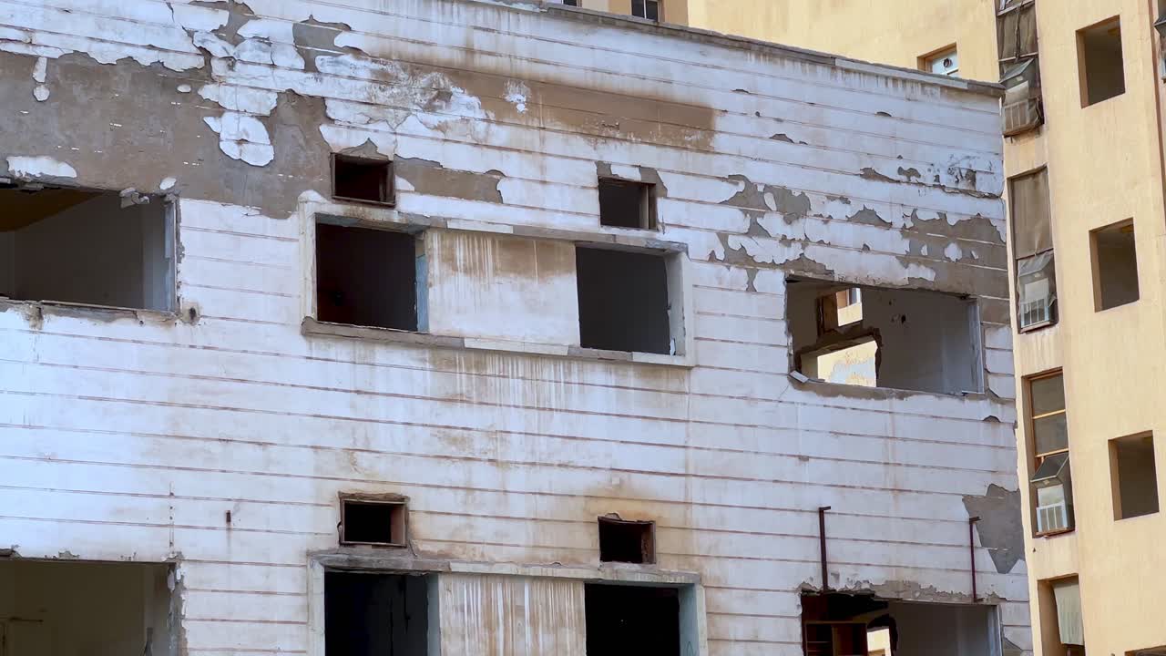 Weathered exterior of derelict building with broken windows and peeling paint. Perfect for urban decay, war zone, or crisis concepts.