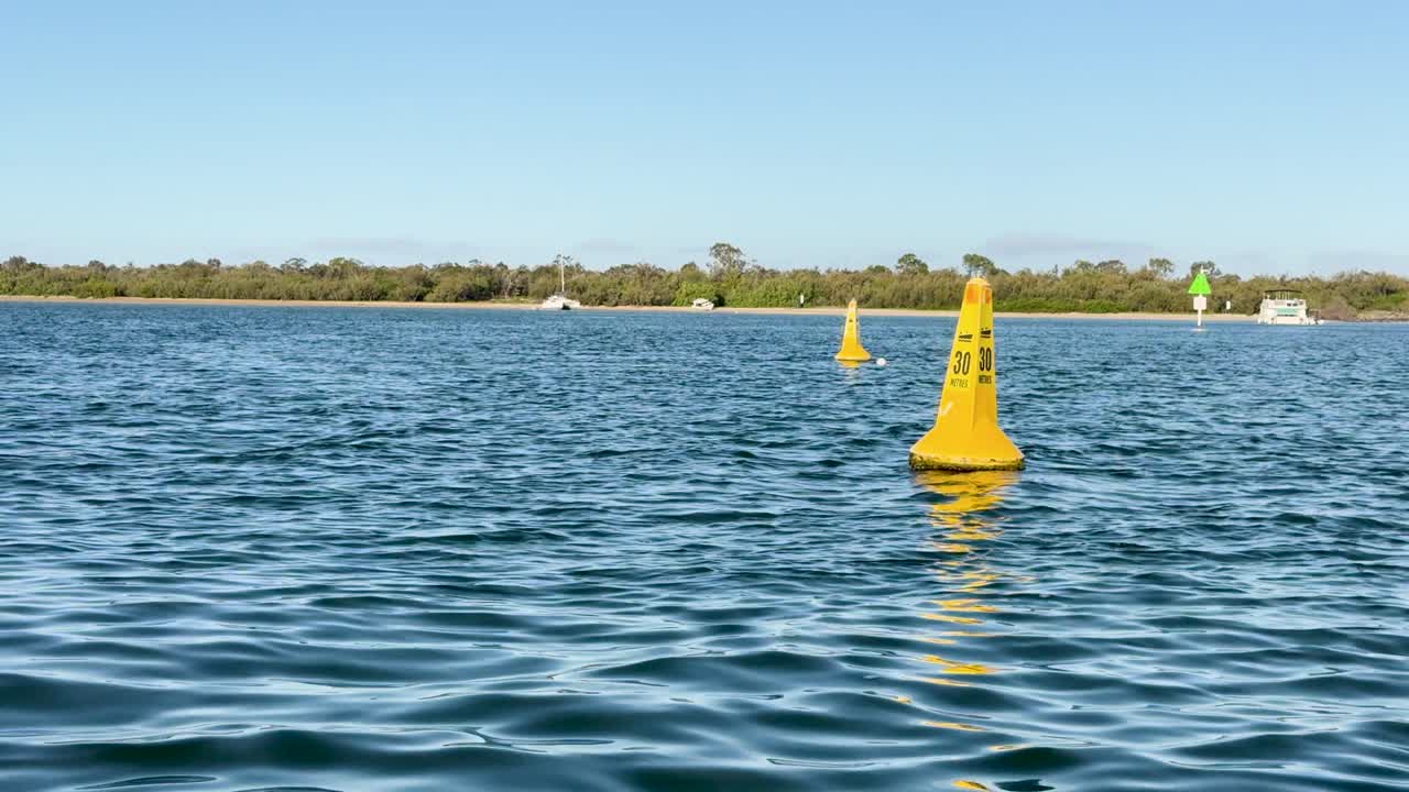 Camera moves steadily toward yellow navigation buoy on calm water under clear daylight sky