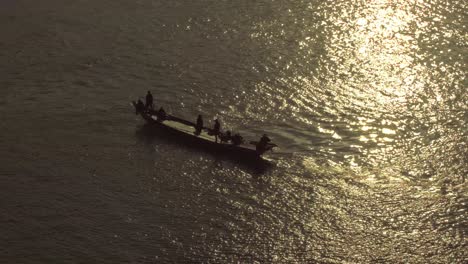 Arial-shot-of-fishing-boat-heading-out-at-sunset-with-people-waving-silhouetted-in-the-evening-sun