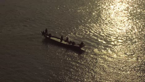 arial shot of fishing boat heading out at sunset with people waving silhouetted in the evening sun