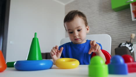 serious caucasian baby boy sits at the white desk. baby boy plays with toy pyramid.