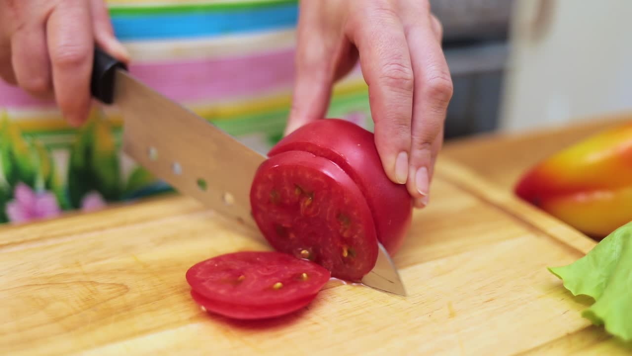 Women's hands Housewives cut with a knife fresh tomato on the cutting Board of the kitchen table