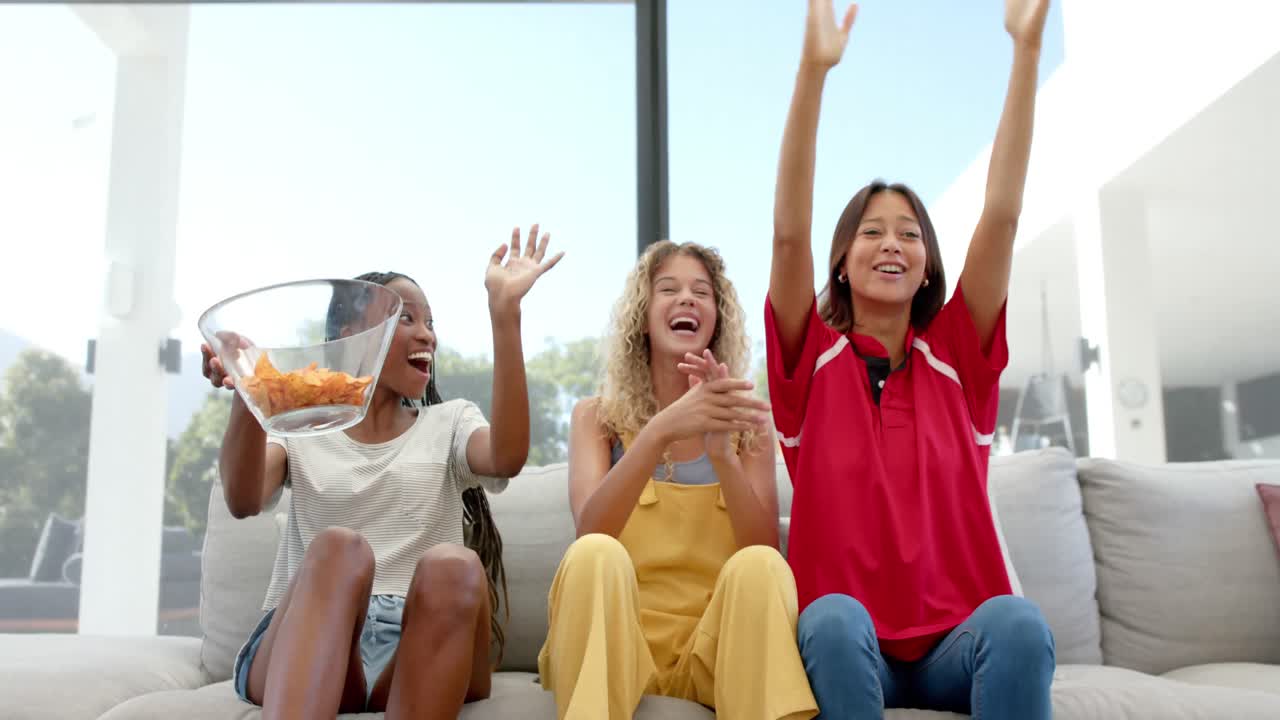 ⁇ 을 가진 행복한 다양한 여성 친구들이 tv에서 스포츠를 보고 응원하고, 느린 동작