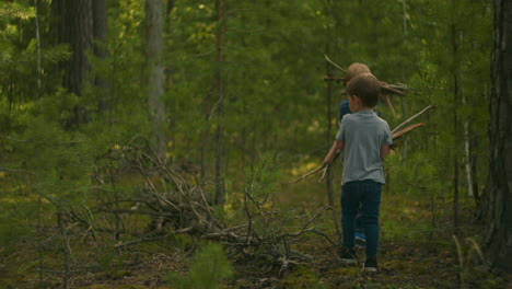 two boys in the woods collect sticks for the fire. 3-6 years of man collect firewood for a fire in the forest