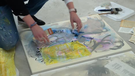 female artist on floor of a busy home studio, layering yellow paper on a canvas