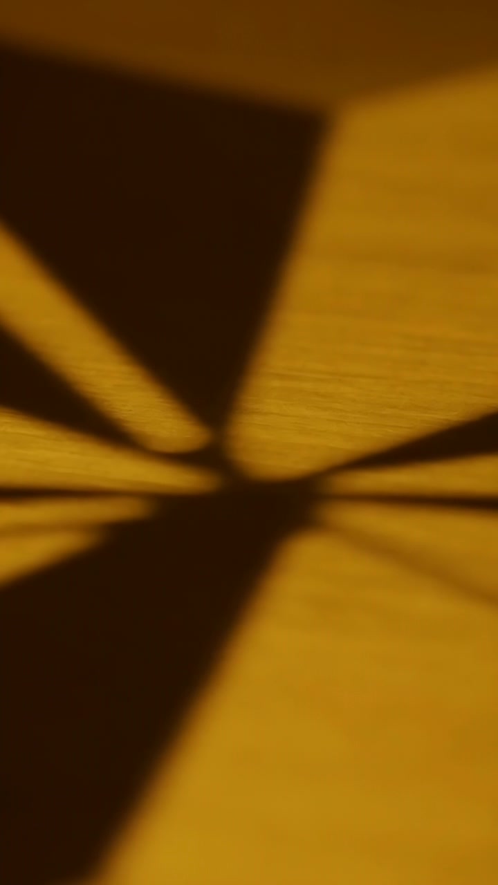 Verticale video: Verschuivend licht werpt spaakschaduwen die over een houten tafel bewegen, veroorzaakt door een ventilator