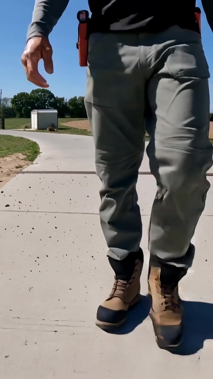 Vertical video: Entering frame, worker going to work in park wearing cargo pants, boots, holster