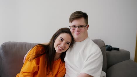 Young-man-with-Down-syndrome-with-his-female-friend-embracing-sit-on-sofa