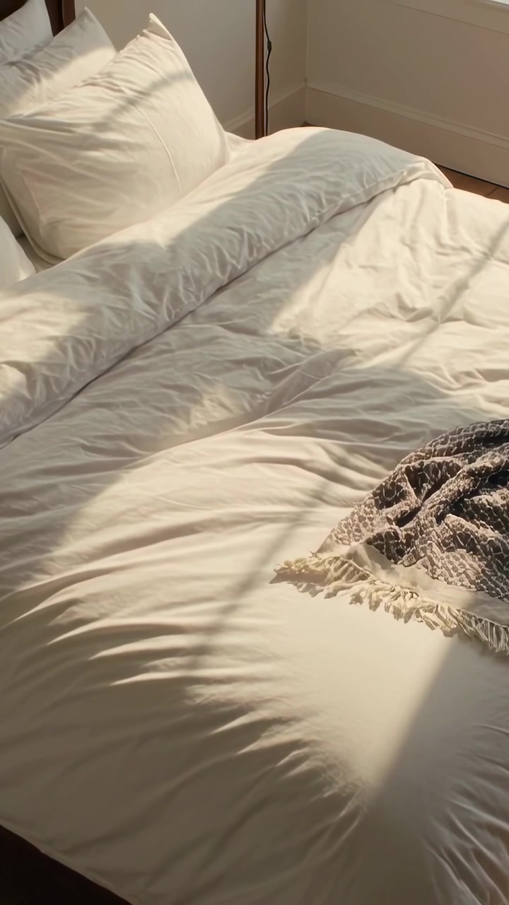 Vertical video: Panning camera revealing made bed in bedroom to showcase duvet, pillows, and lamp