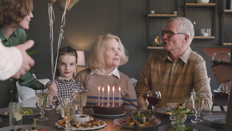 senior woman blowing out candles on birthday cake during a celebration with her family at home