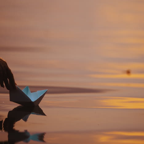 origami boat on evening water background. hand lets paper boat down into the water at sunset. close-up.
