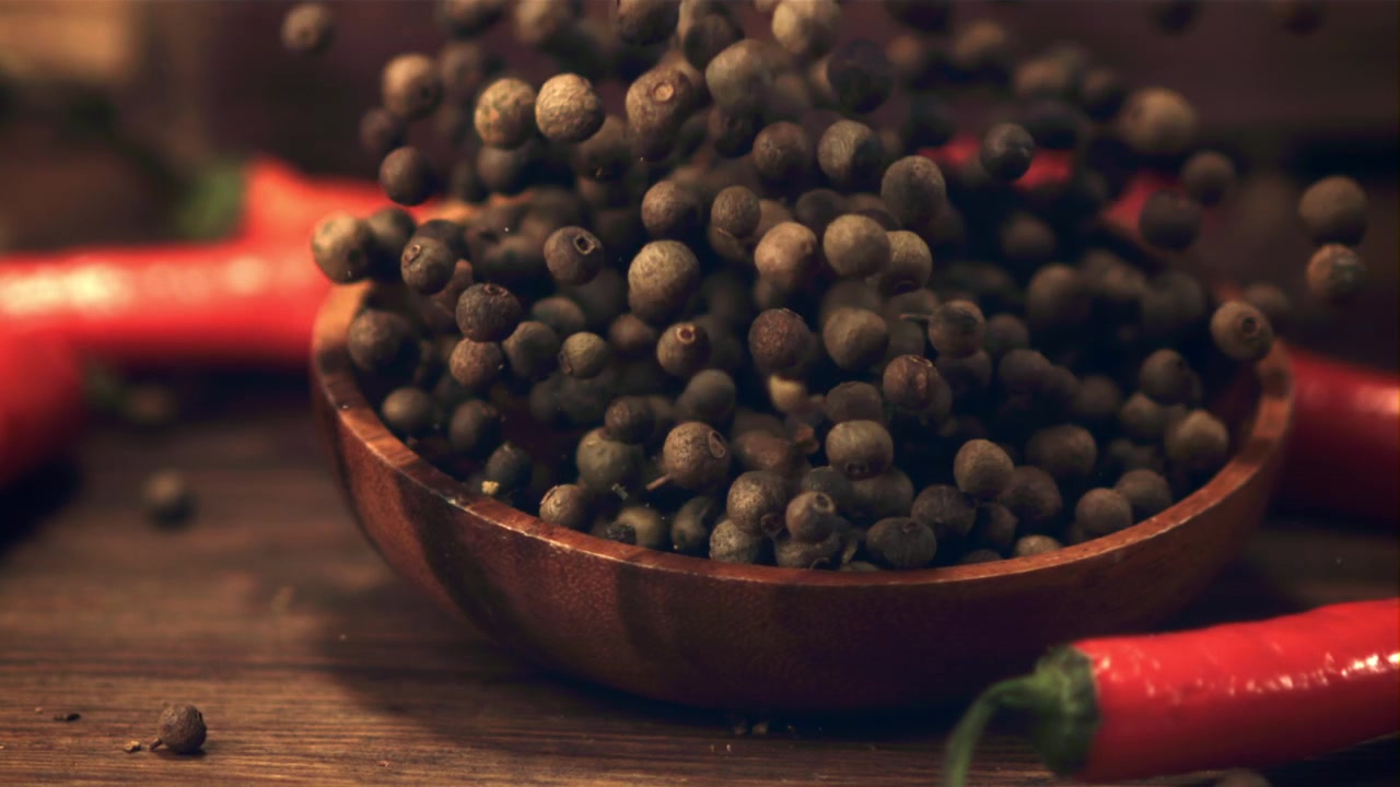 Granos de pimienta cayendo a cámara lenta en un cuenco de madera con chiles