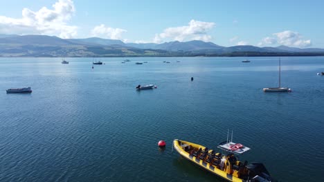 Snowdonia-Clear-Mountain-Range-Luftbild-Mit-Booten-Auf-Sonniger,-Ruhiger,-Walisischer,-Schimmernder-Meereslandschaft