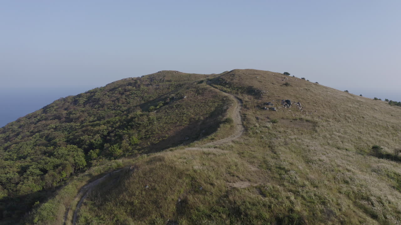 Sorvolo della strada in cima al crinale su alture con campi verdi vicino alla costa oceanica, in una giornata luminosa, limpida e soleggiata.