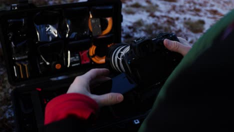 Guy-setting-up-large-DLSR-camera-with-tele-lens-flipping-screen,-flight-case-with-equipment,-close-up