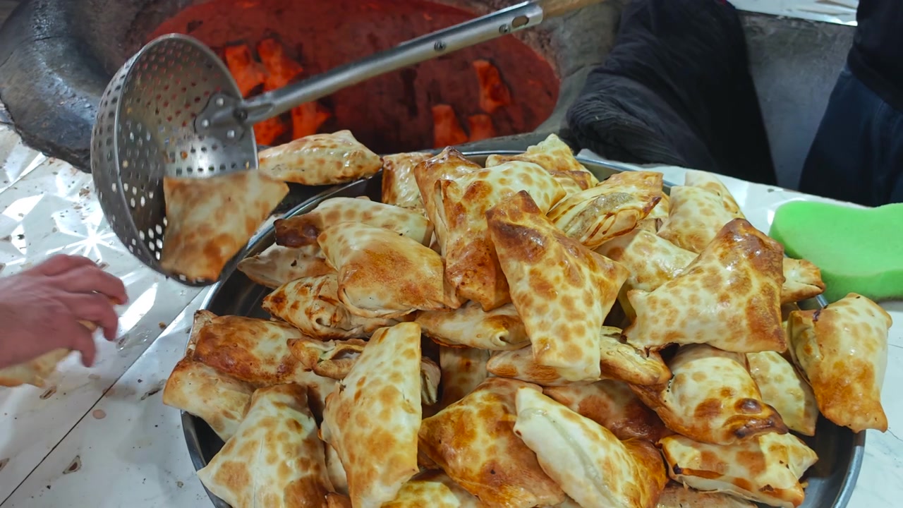Panettiere che prepara pasticcini Samsa freschi in un tradizionale forno tandoor