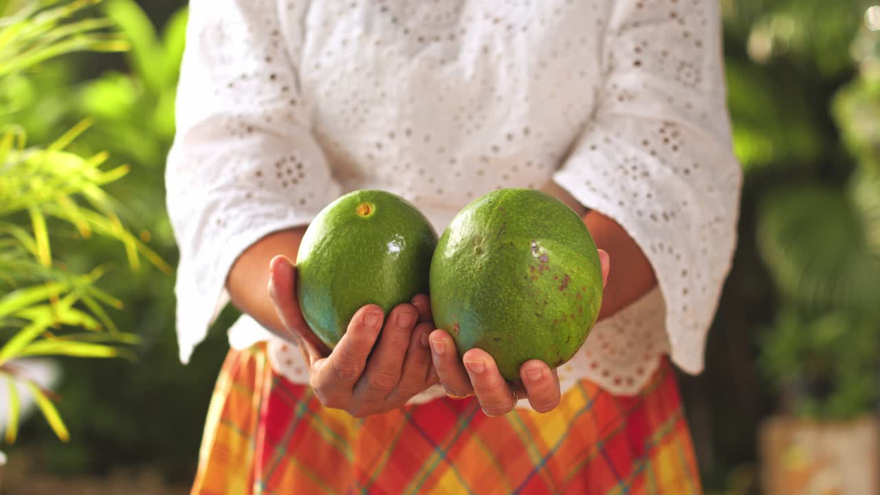 mujer con camisa blanca y falda a cuadros mostrando aguacates a la cámara