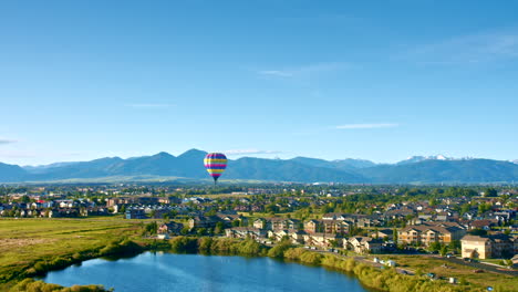 Montañas-Con-Globo-Aerostático-Volando-Al-Amanecer-Sobre-El-Estanque-De-La-Ciudad---Amplia-Vista-Aérea