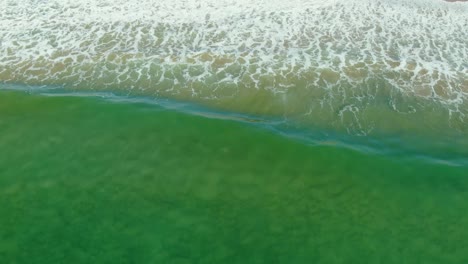 drone aéreo siguiendo las olas que chocan contra la playa