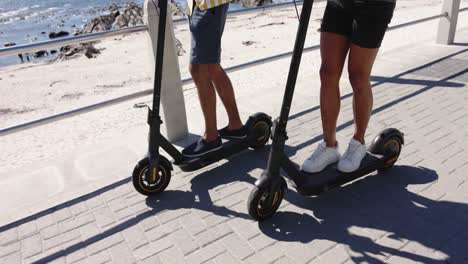 happy diverse gay male couple using scooters at promenade by the sea, slow motion