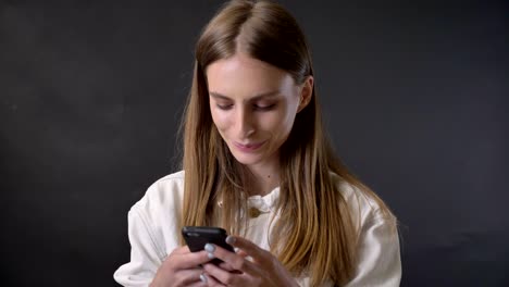 Young cool girl is tying message on smartphone, tucking hair, communication concept, grey background