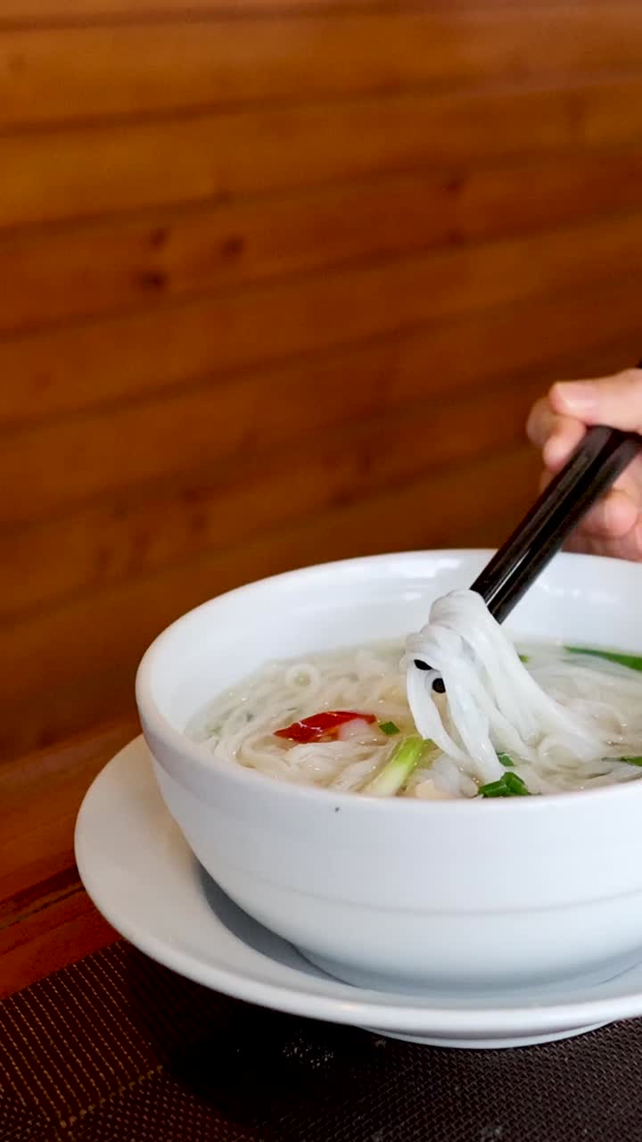 persona comiendo sopa de fideos con palillos en una mesa