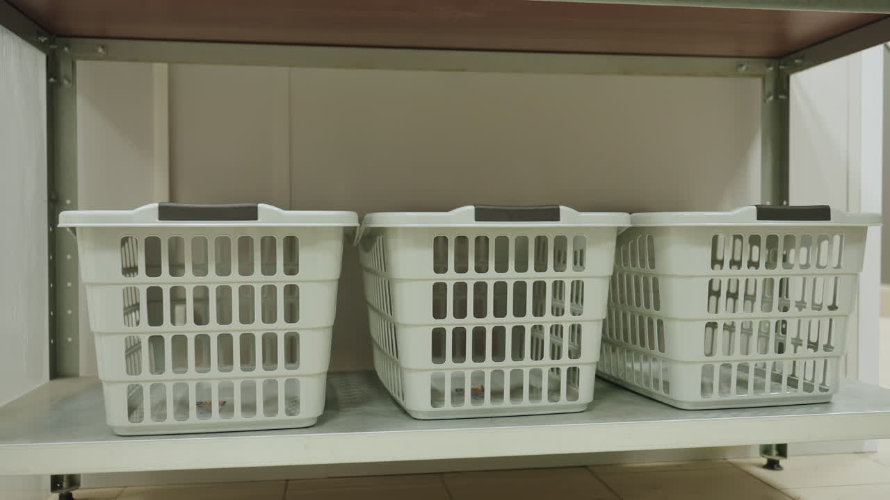 Three white laundry baskets lined on metal shelf in tidy laundromat room, empty containers ready for service, clean utility interior shows symmetry, order, organization, tiled floor