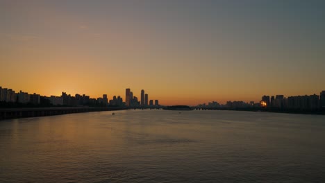 Aerial-view-over-Han-river-and-Seoul-city-skyline-cityscape-with-high-buildings-in-silhouette-mood-at-orange-sunset-time