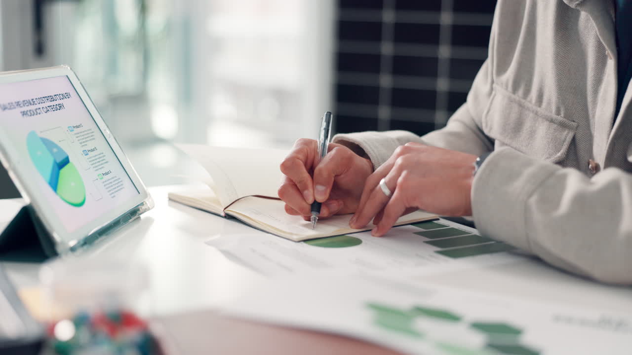 Close-up of Person's Hands Writing Notes in a Notebook at a Desk