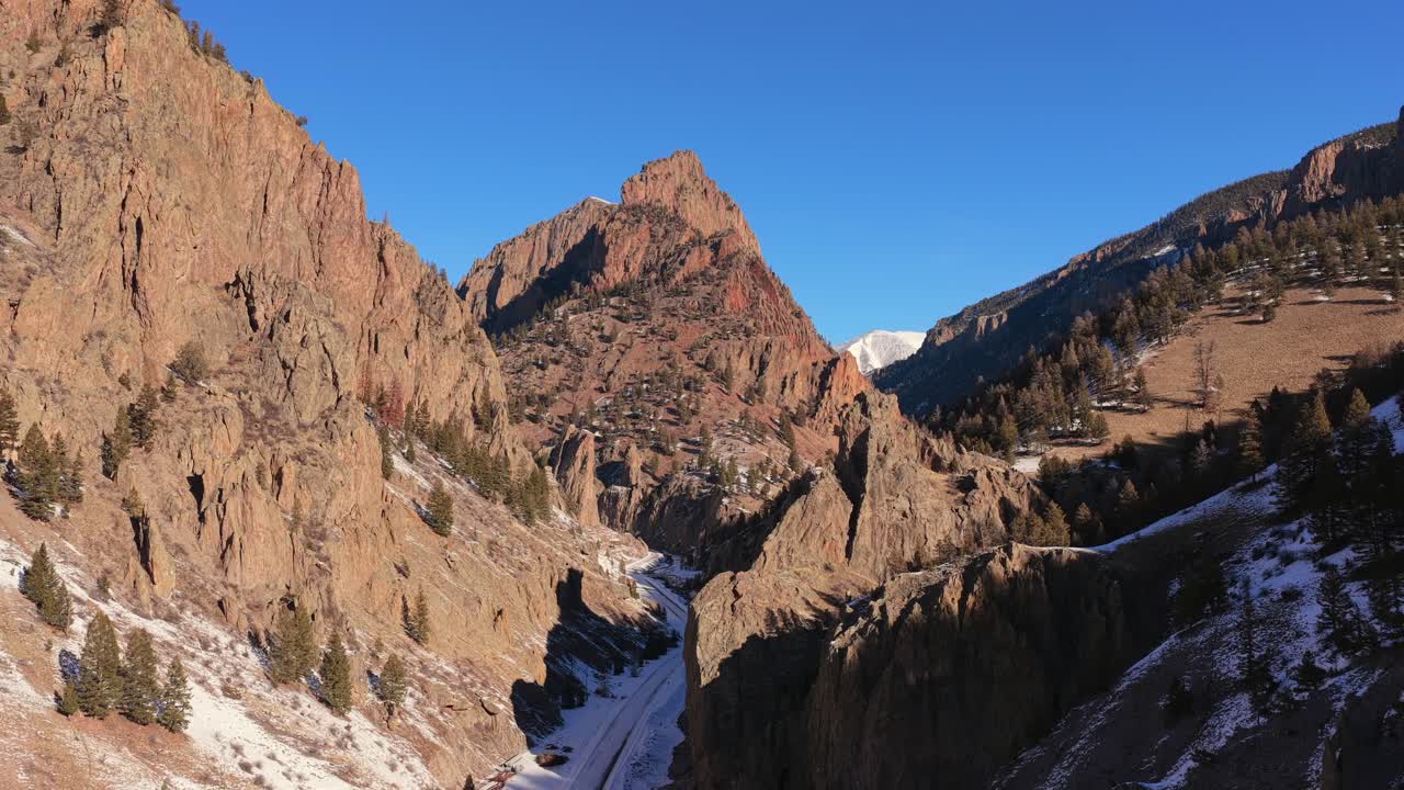 Una ripresa aerea cinematografica cattura una vetta di montagna appuntita che si erge tra ripide pareti rocciose del canyon. Ombre profonde e drammatiche e la neve invernale mettono in risalto l'immensa scala di questo aspro territorio montano.