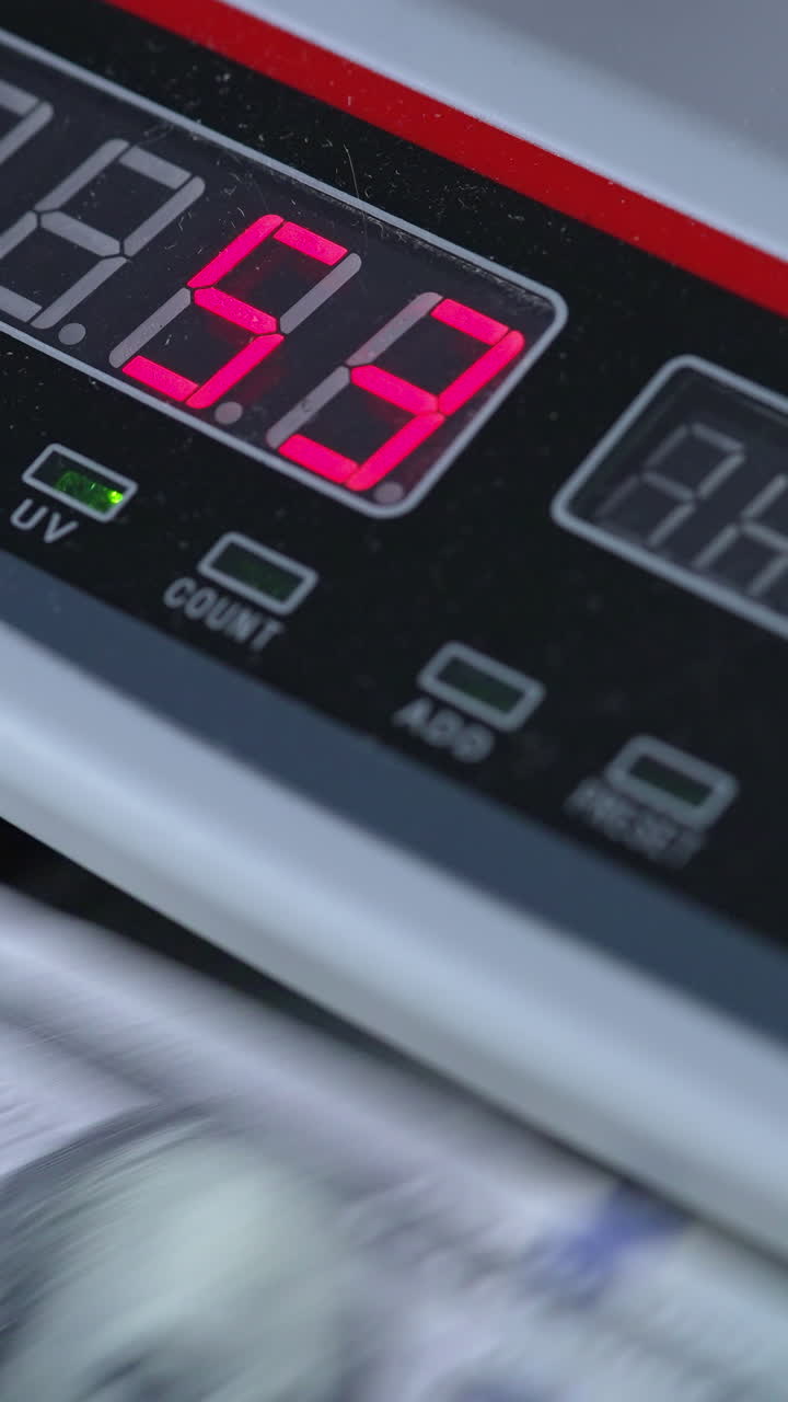 Electronic scoreboard of cash counting machine with numbers on. Dollar bills rotating in the device. Close up. Vertical video