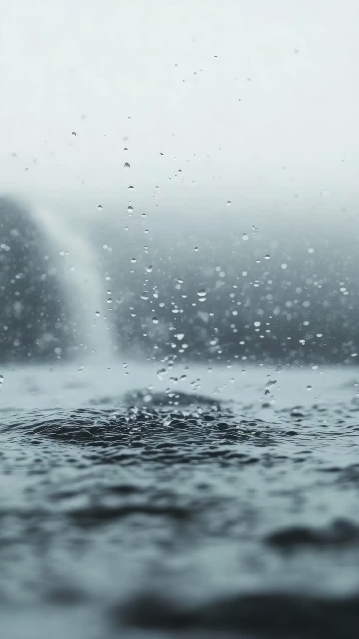 Close-up, low-angle shot capturing raindrops splashing on a surface, creating a serene and calming