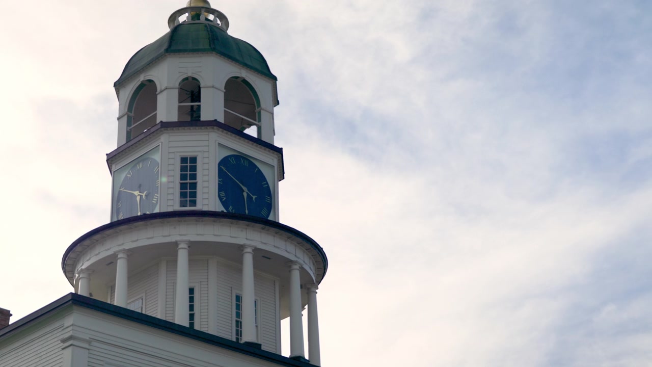 A torre do relógio está localizada em Halifax, Canadá. Ela possui mostradores azuis e uma cúpula verde no topo. O céu é visível atrás da torre. A cena mostra um dia claro