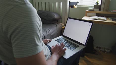 hombre caucásico usando computadora portátil, sosteniendo su barbilla en el dormitorio