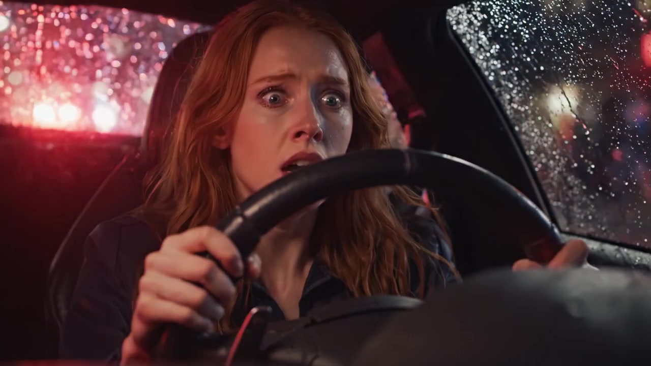 Ansiedad y tensión amplificadas: la reacción temerosa de un personaje mientras conduce en una escena nocturna lluviosa entre luces de policía y reflejos.