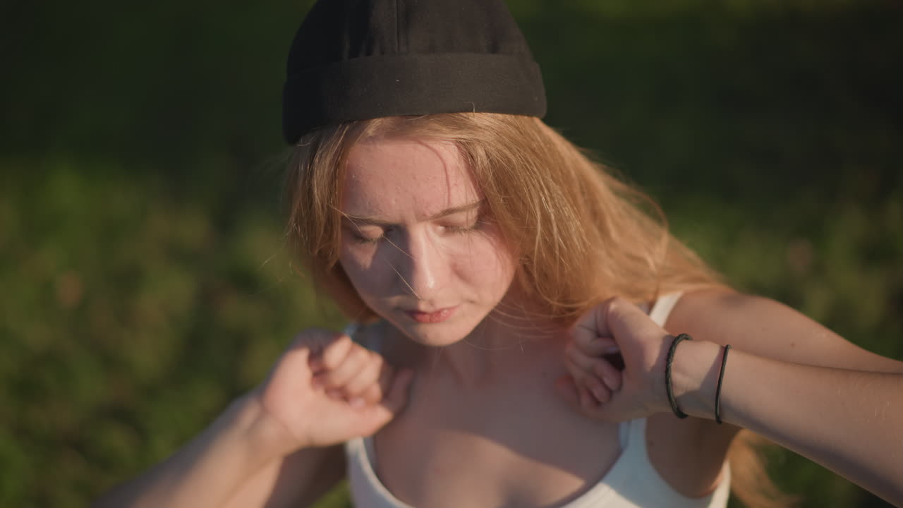 Кавказская женщина танцует на улице в парке, солнечный свет, кепка, жестикуляция и ритмичные движения фристайла, крупный и широкий план, непринужденный смех, атмосфера репетиции, летняя трава на заднем плане, выразительные руки, бодрый темп