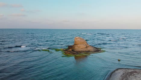 Aerial-panning-shot-around-cliff-in-the-sea-at-sunset