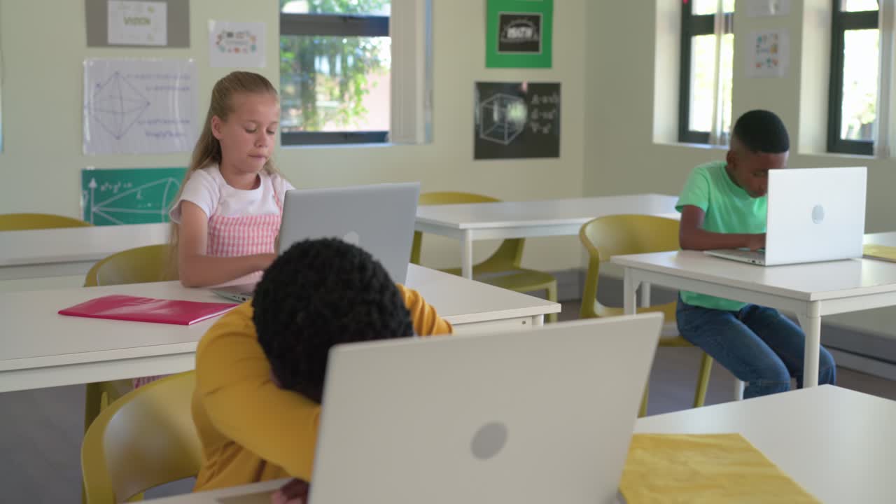 Diverse classmates in classroom with center female glancing up after looking down, typing on laptop
