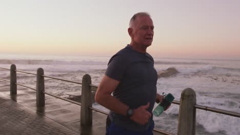 Senior-man-with-water-bottle-running-on-the-promenade