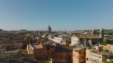 Forwards-fly-above-old-apartment-houses-in-historic-city-centre.-Multistorey-residential-buildings-with-rooftop-terraces-at-golden-hour.-Heading-to-tower-of-San-Carlo-al-Corso-basilic.-Rome,-Italy