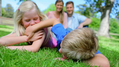 brother and sister tickling each other while lying in the grass