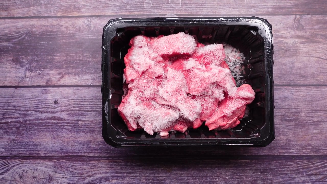 Frozen Raw Meat Chunks in a Black Plastic Container
