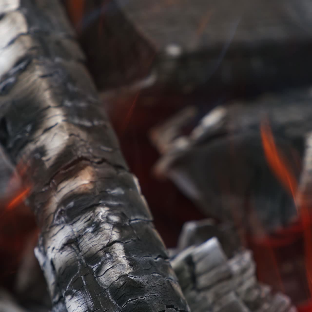 Wooden embers glowing in fire. Smoldered logs burning in fire. Motion of fire tongues over charcoals. Close-up.