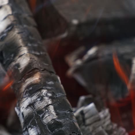 wooden embers glowing in fire. smoldered logs burning in fire. motion of fire tongues over charcoals. close-up.