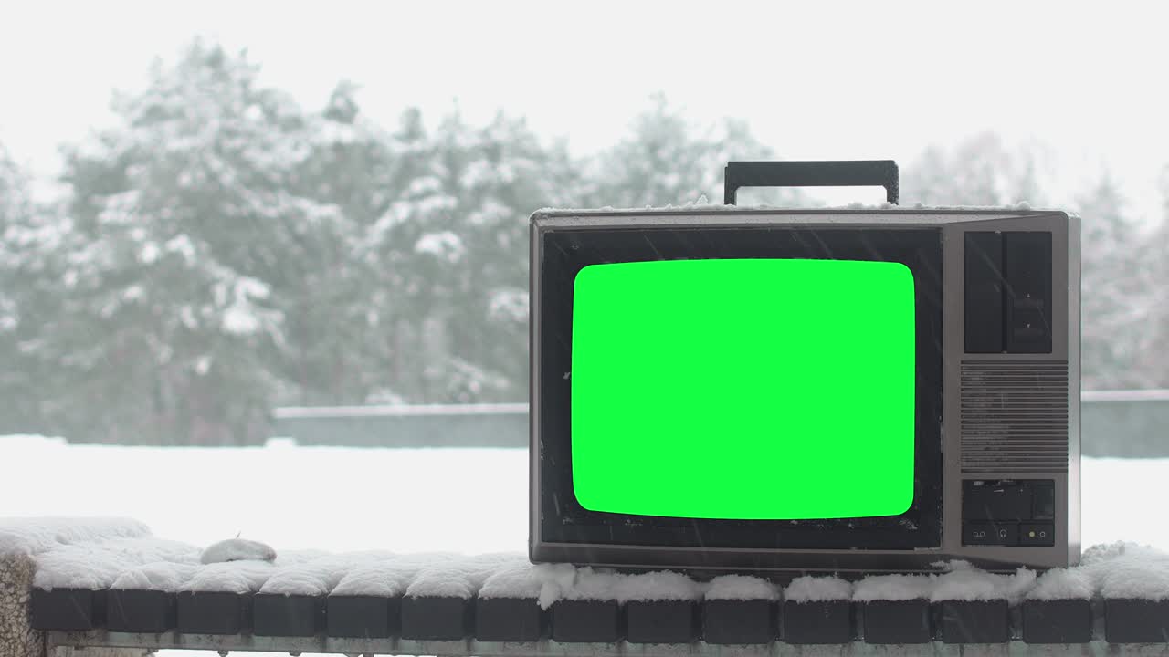 Vintage tv with green screen on bench covered by snow in winter season