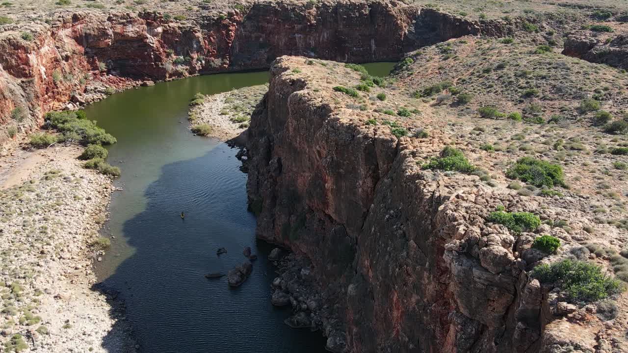 toma aérea de pájaros de una persona remando con sup en el río verde rodeado de paredes de acantilados gigantes