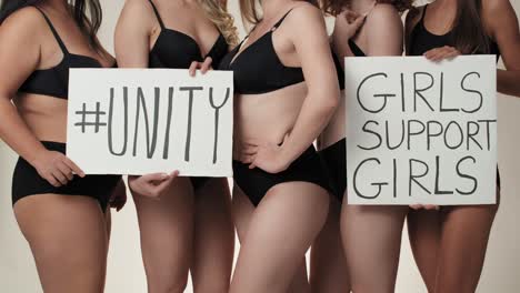 grupo de mujeres irreconocibles vestidas con ropa interior y de pie en el estudio con una pancarta.